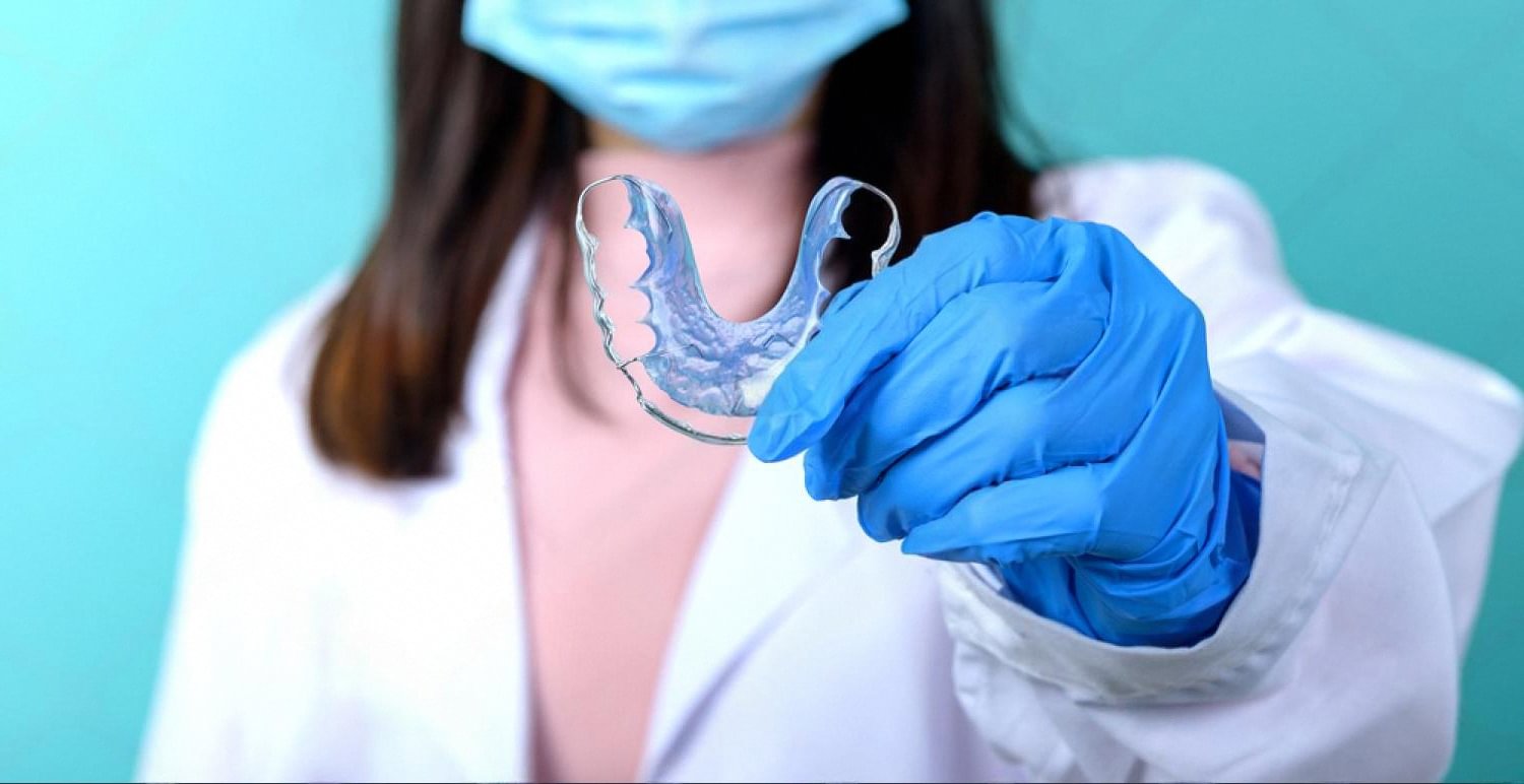 Dentist in gloves holding a clear Invisalign aligner tray during a UAE consultation